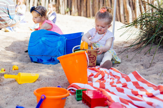 A toddler is sitting in a sandpit playing with a bucket and spade.