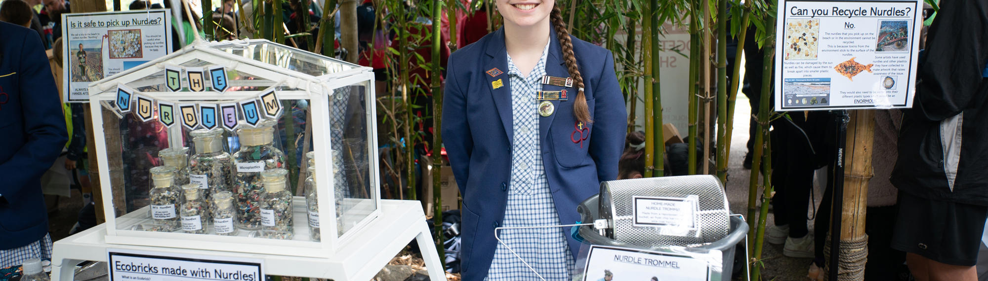 A school student stands in front of a craft showcase