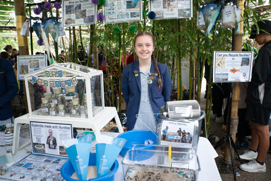 A school student stands smiling behind her craft Schools showcase, featuring nurdles.