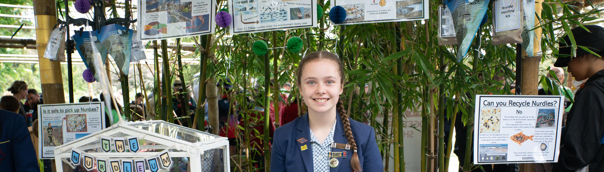 A school student stands smiling behind her craft Schools showcase, featuring "nurdles."