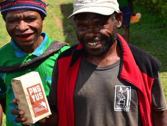 Two smiling Guineans, one looking to the camera while holding a bag of locally produced coffee.