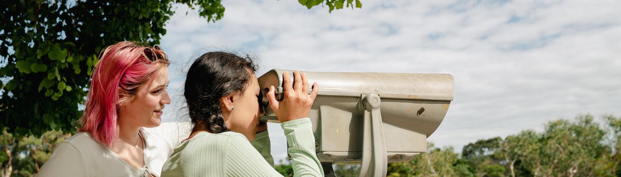 Side view of two students as they look to the right through lookout binoculars
