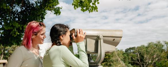 Side view of two guests as they look to the right through lookout binoculars.