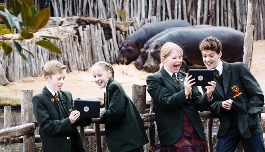 Four students with two tablets in front of three Hippopotamuses.