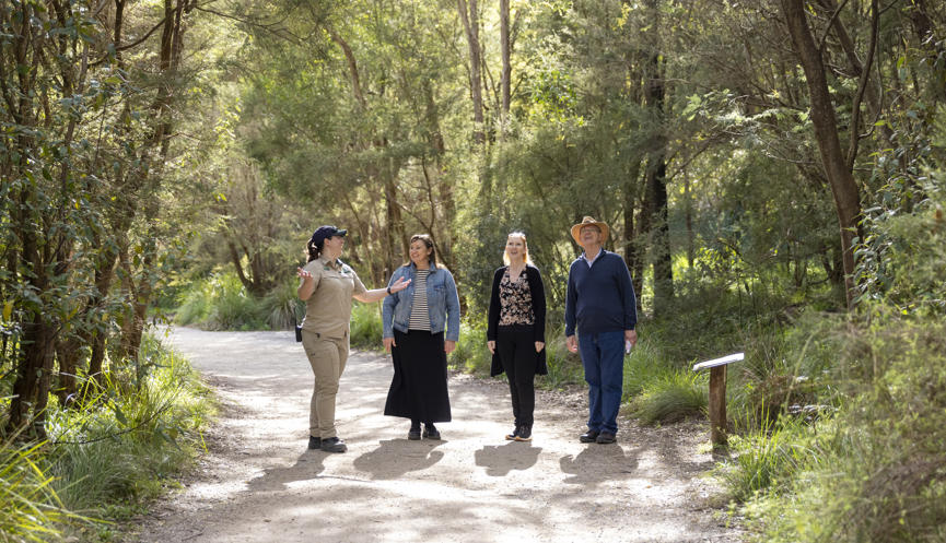 Keeper escorting and conversing with three guests on a woodland path.