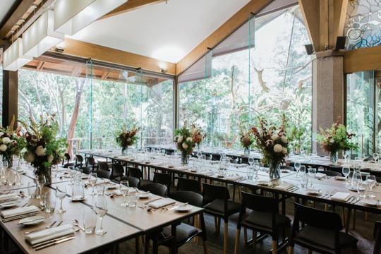 View of the Rainforest Room, prepped for a ceremony with flowers, lights, rowed tables and chair.
