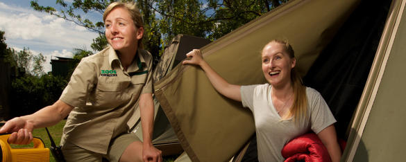 A woman lifts the door of a tent and smiles as a zoo staff members squats next to her holding a torch