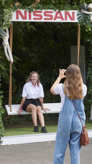 One woman taking photo of a friend who is seating on a Nissan swing chair, adorned by plush animals.