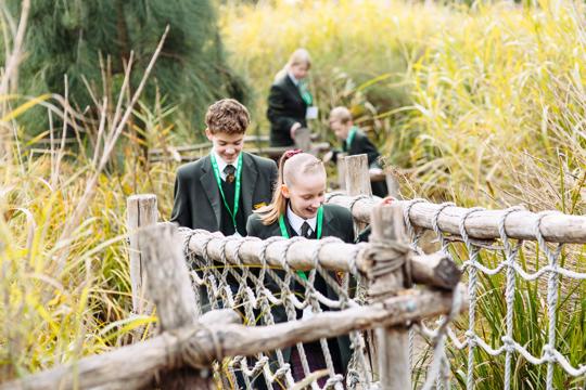 Two children, a boy and a girl, in school uniform are walking across a wooden bridge, smiling