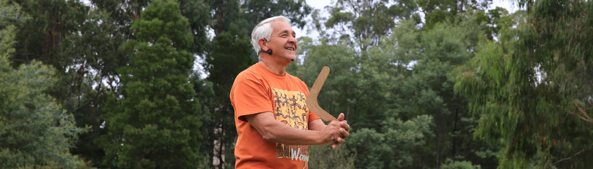 Elder Murrundindi at Healesville Sanctuary, making a speech with microphone while holding a boomerang up by the end.