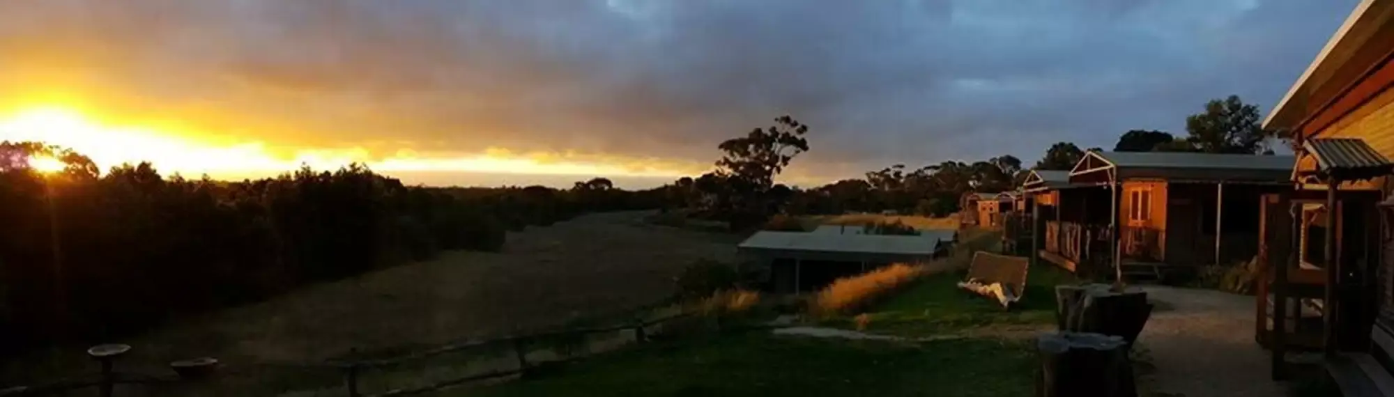 A row of huts - on the right - overlooking a valley at sunset - to the left.