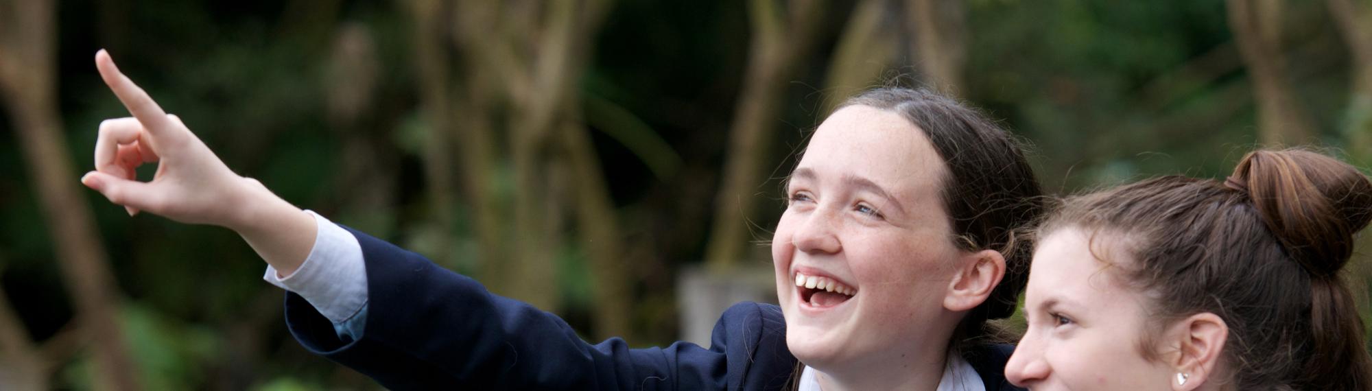 Two students look excitedly at something out of frame, one pointing left.