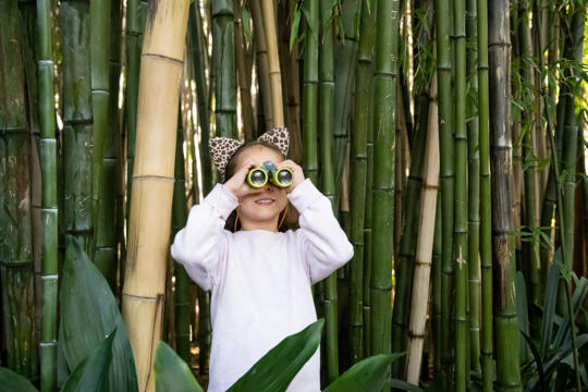 Young guest holding pair of binoculars and smiling enthusiastically, against the Bamboo Forest.