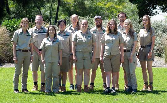 A team of zoo employees stand in a row on the grass smiling