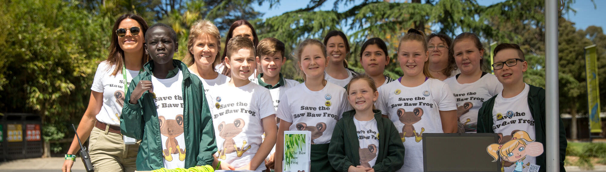 Group of eleven students and three Zoo staff, standing in a row, smiling and wearing shirts saying "Save the Baw Baw Frog."