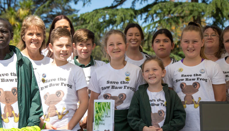 Group of eleven students and three Zoo staff, standing in a row, smiling and wearing shirts saying "Save the Baw Baw Frog."