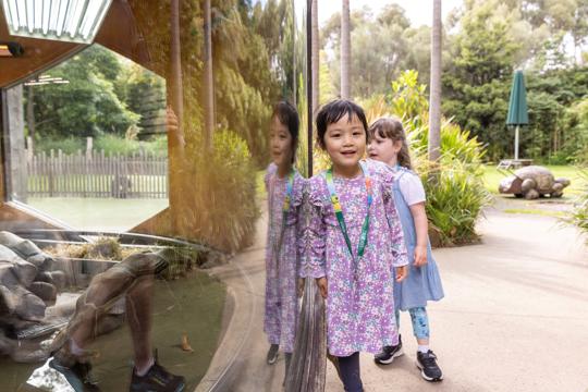 Two girls at Growing Wild habitat. One girl is looking at the camera and another girl is looking at Giant Tortoise