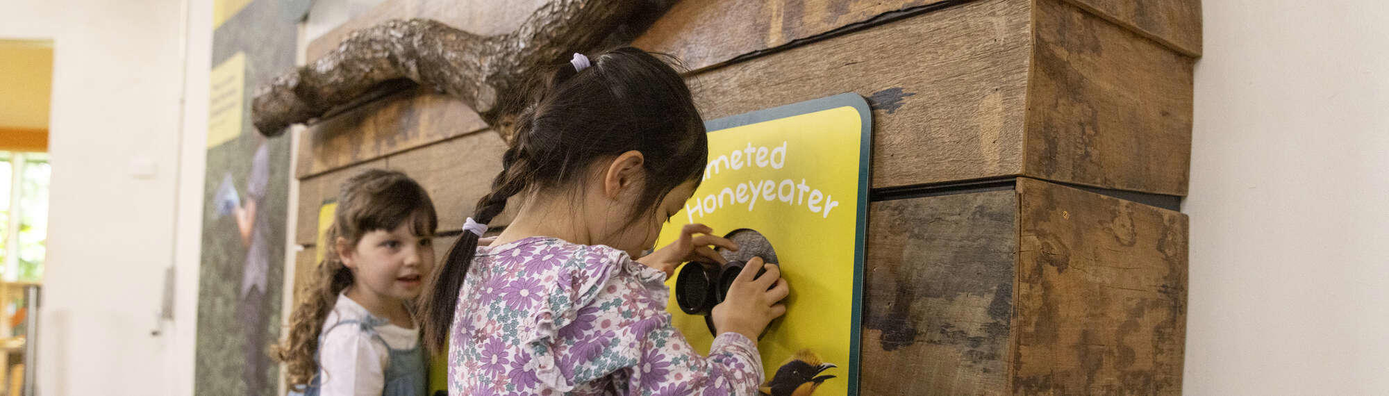 Two young guests at the Helmeted Honey-eater binoculars of Keeper Kids, both looking right.