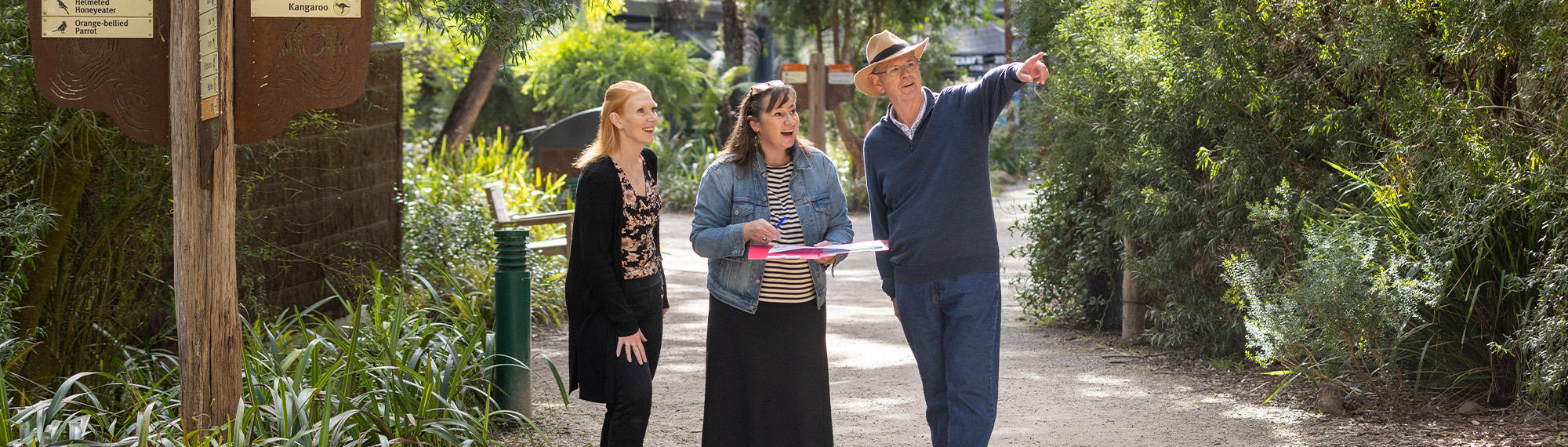 Three guests taking part in Healesville Sanctuary's Run Around the Zoo, one pointing right and another holding a blue pen and paper.