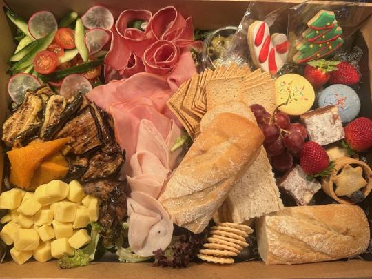 Hamper of assorted foods, including ham, turkey, cheese, zucchini, pastrami, tomato, olives, bread, cherries, strawberries, cookies and macarons.