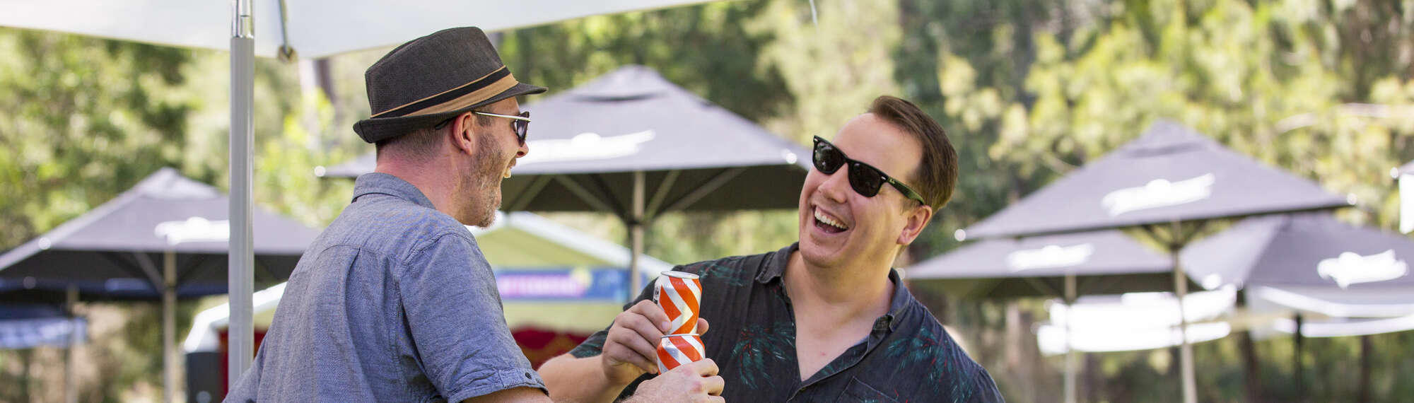 Two visitors to Acoustic Afternoon bump their orange-silver cans together while laughing.