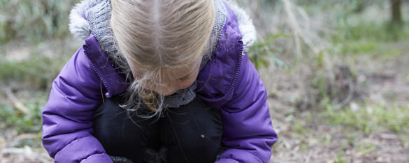 A young girl in a purple jacket bending down on the ground.