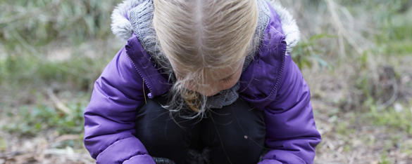 A young girl in a purple jacket bending down on the ground.
