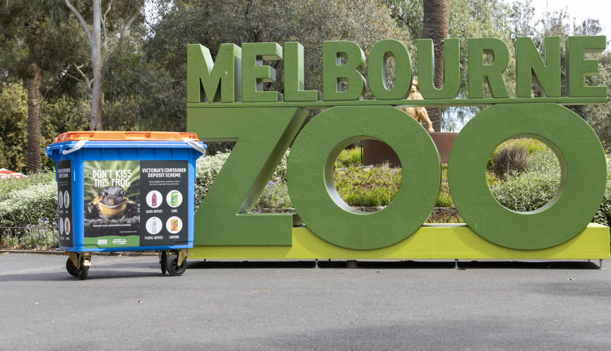 "Don't kiss this Frog, donate your drink containers instead" - A recycling skip with this text on front stands next to the green Melbourne Zoo sign.