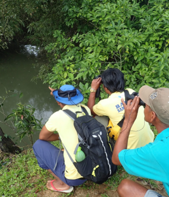 Group of three men looking into a river with binoculars.