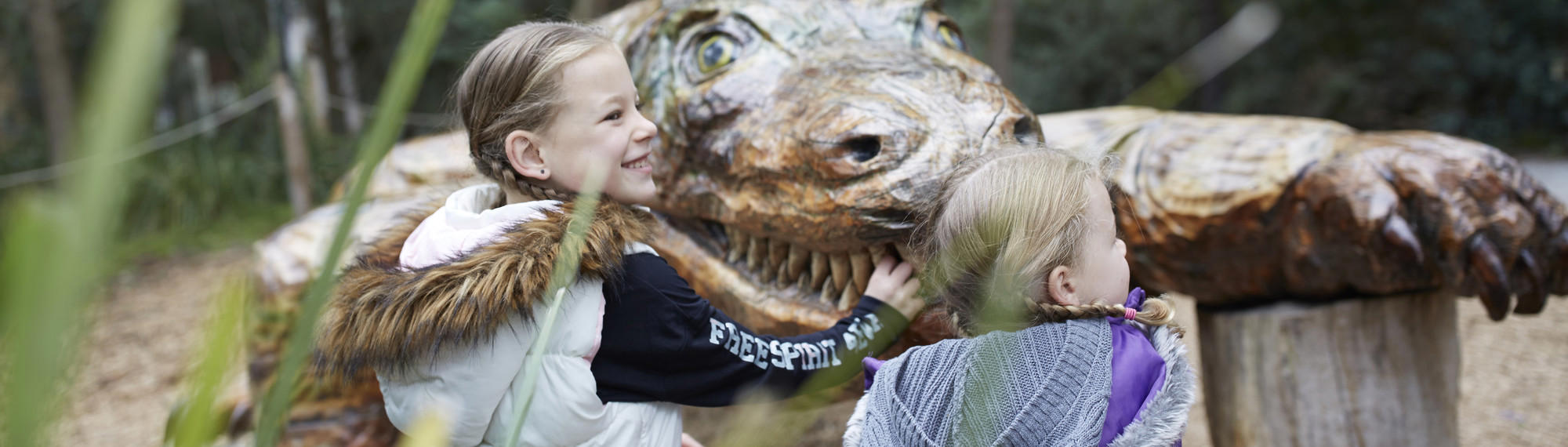 Two kids playing at Healesville Sanctuary, with Megalania (the wood-carve statue) in the background.
