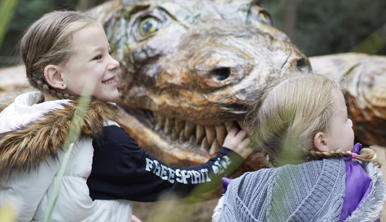 Two kids playing at Healesville Sanctuary, with Megalania (the wood-carve statue) in the background.