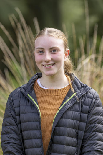 Portrait of Youth Advisor Zoe, smiling to the camera against a leafy backdrop.