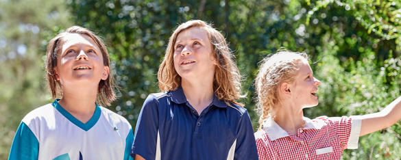 Three students smile as they walk through the bush on a sunny day