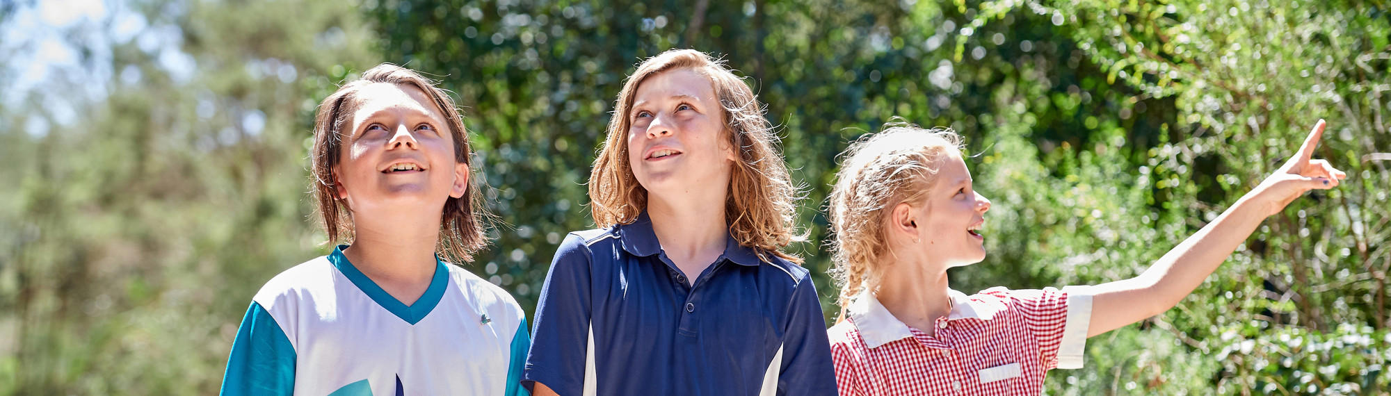 Three students smile as they walk through the bush on a sunny day.