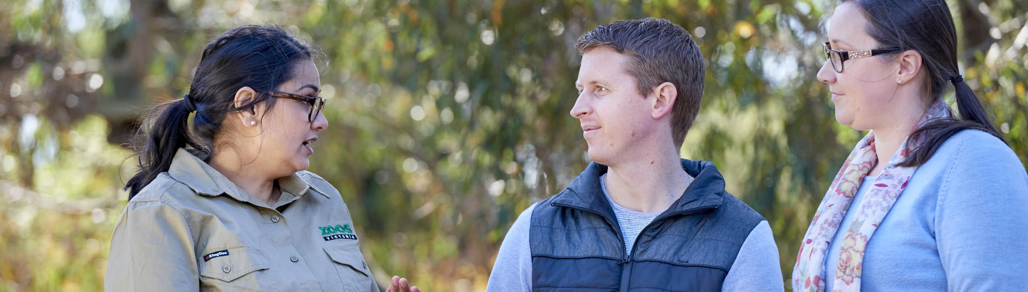 A Zoo staff member stands and talks to two other adults.