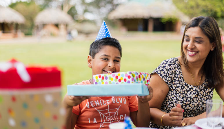 Families with kids enjoying a birthday party celebration picnic at a table on the Village Lawn.